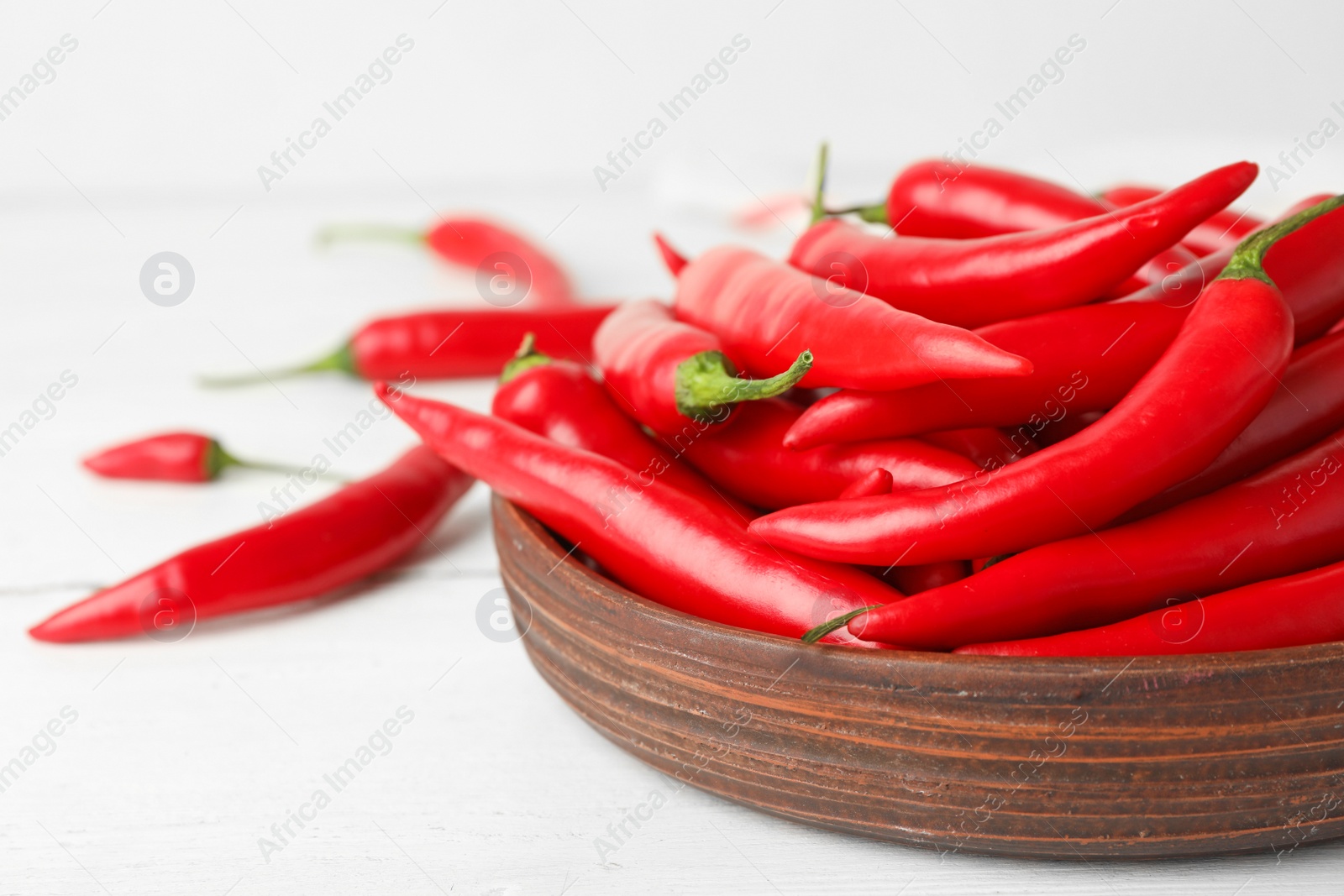 Photo of Wooden bowl with red hot chili peppers on white table, closeup. Space for text