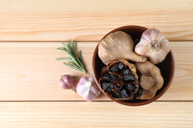 Photo of Bulbs of fresh and fermented black garlic on wooden table, flat lay. Space for text