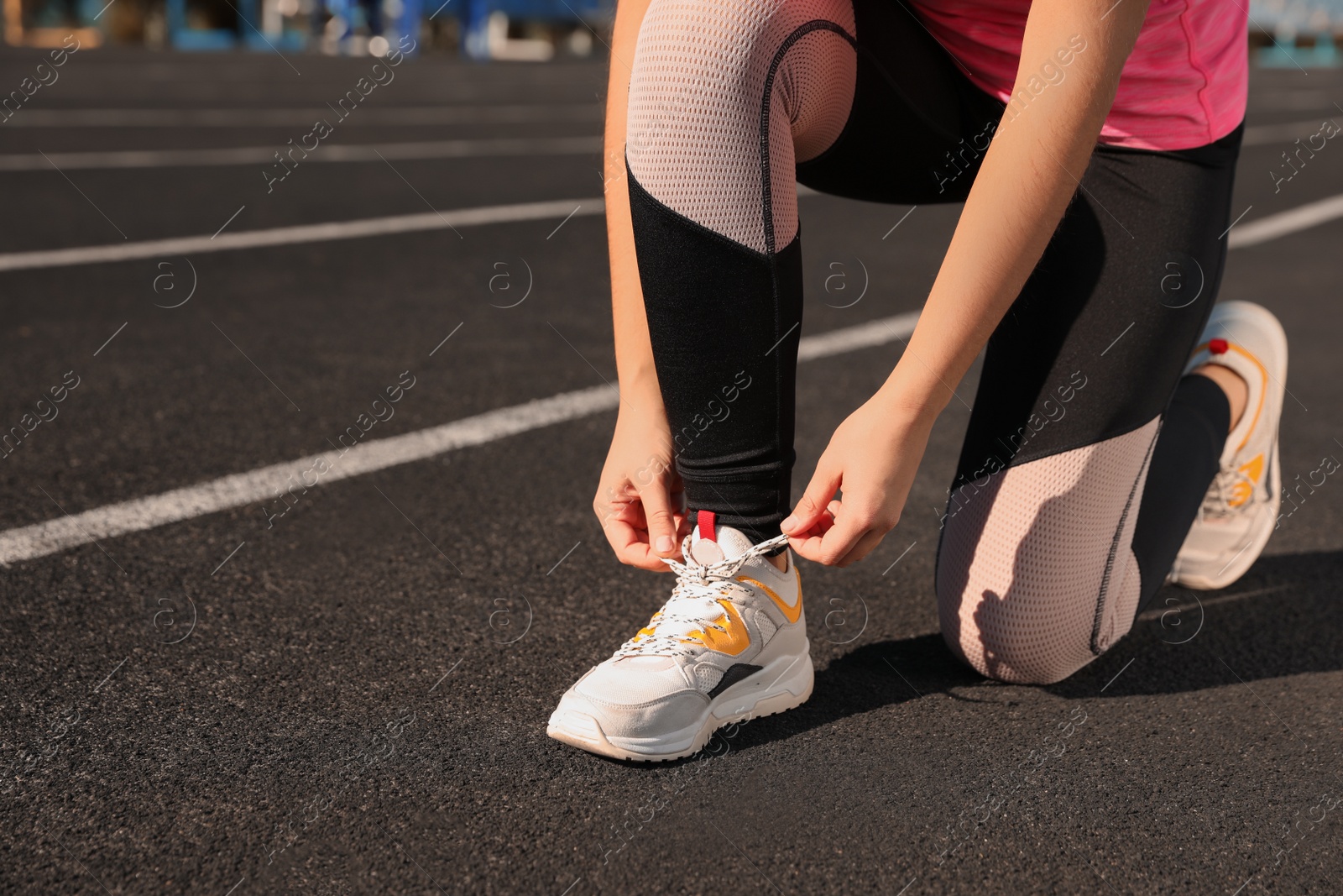 Photo of Young woman tying shoelaces at stadium on sunny day