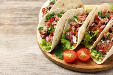 Photo of Delicious tacos with meat and vegetables on wooden table, closeup. Space for text