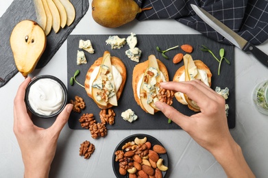 Woman preparing delicious bruschettas with cheese, pear and nuts at table, top view