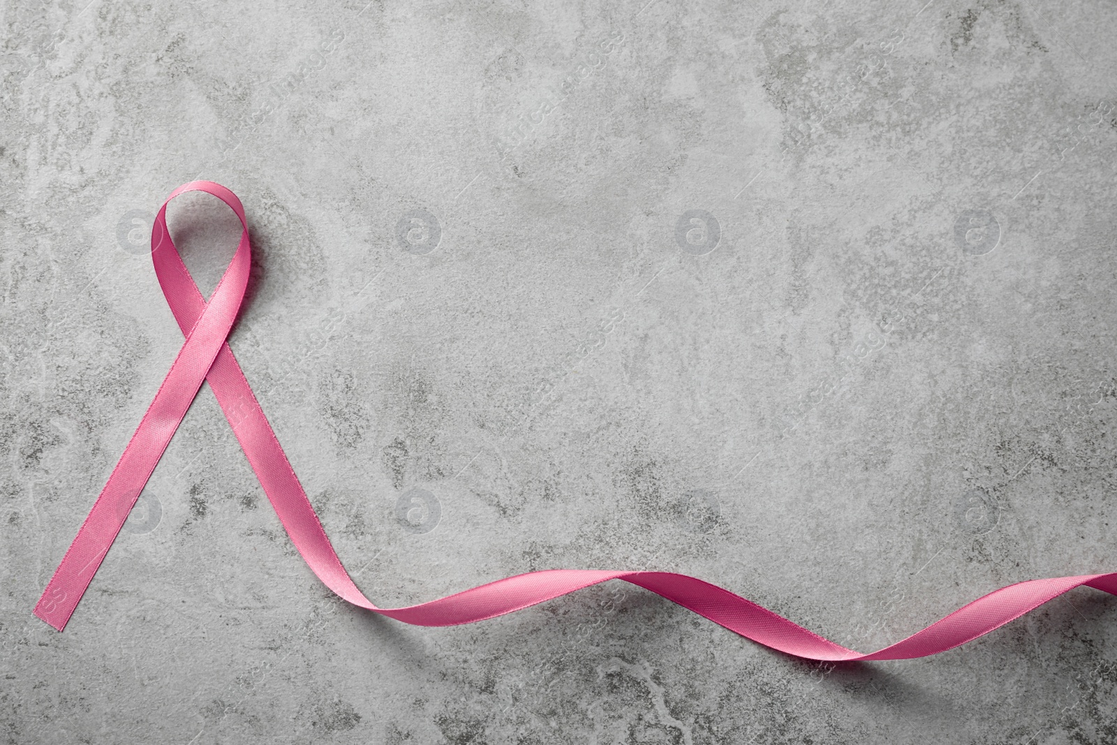 Photo of Pink ribbon on grey table, top view with space for text. Breast cancer awareness concept