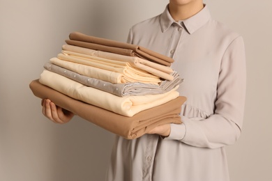 Woman holding stack of clean bed linens on beige background