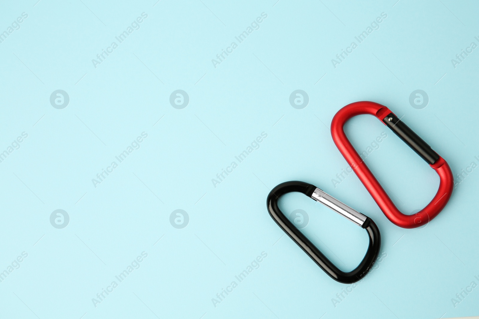 Photo of Two metal carabiners on light blue background, flat lay. Space for text