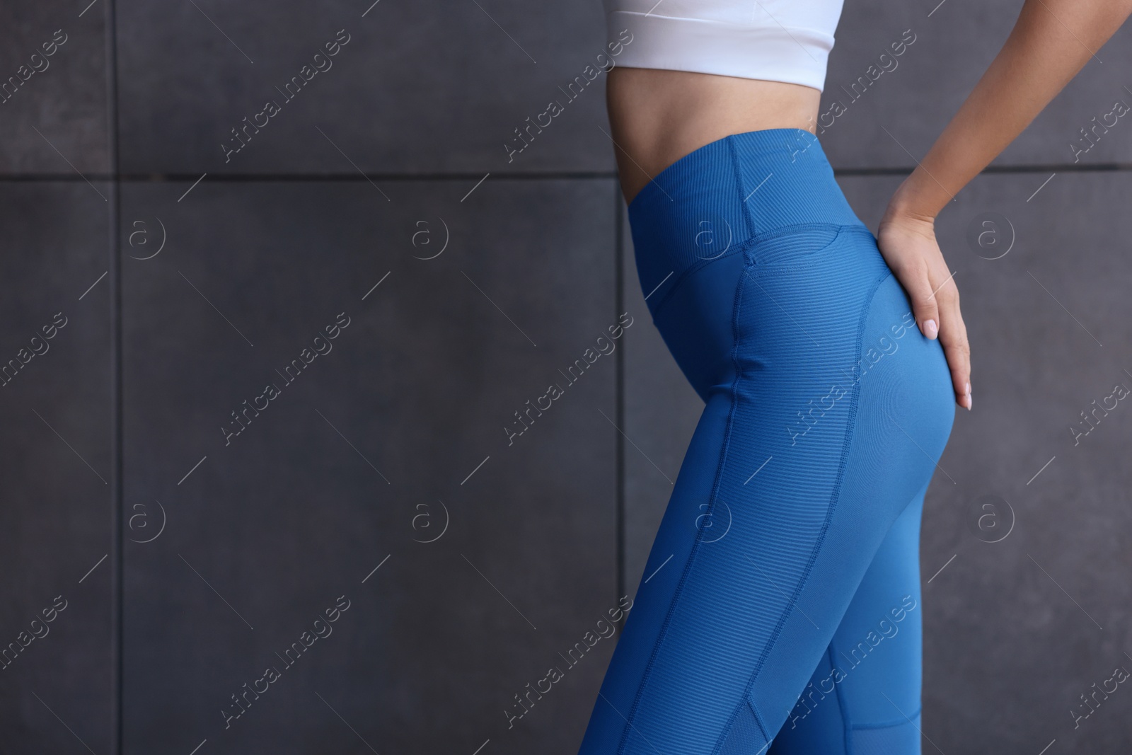 Photo of Woman in sportswear near dark grey wall, closeup. Space for text