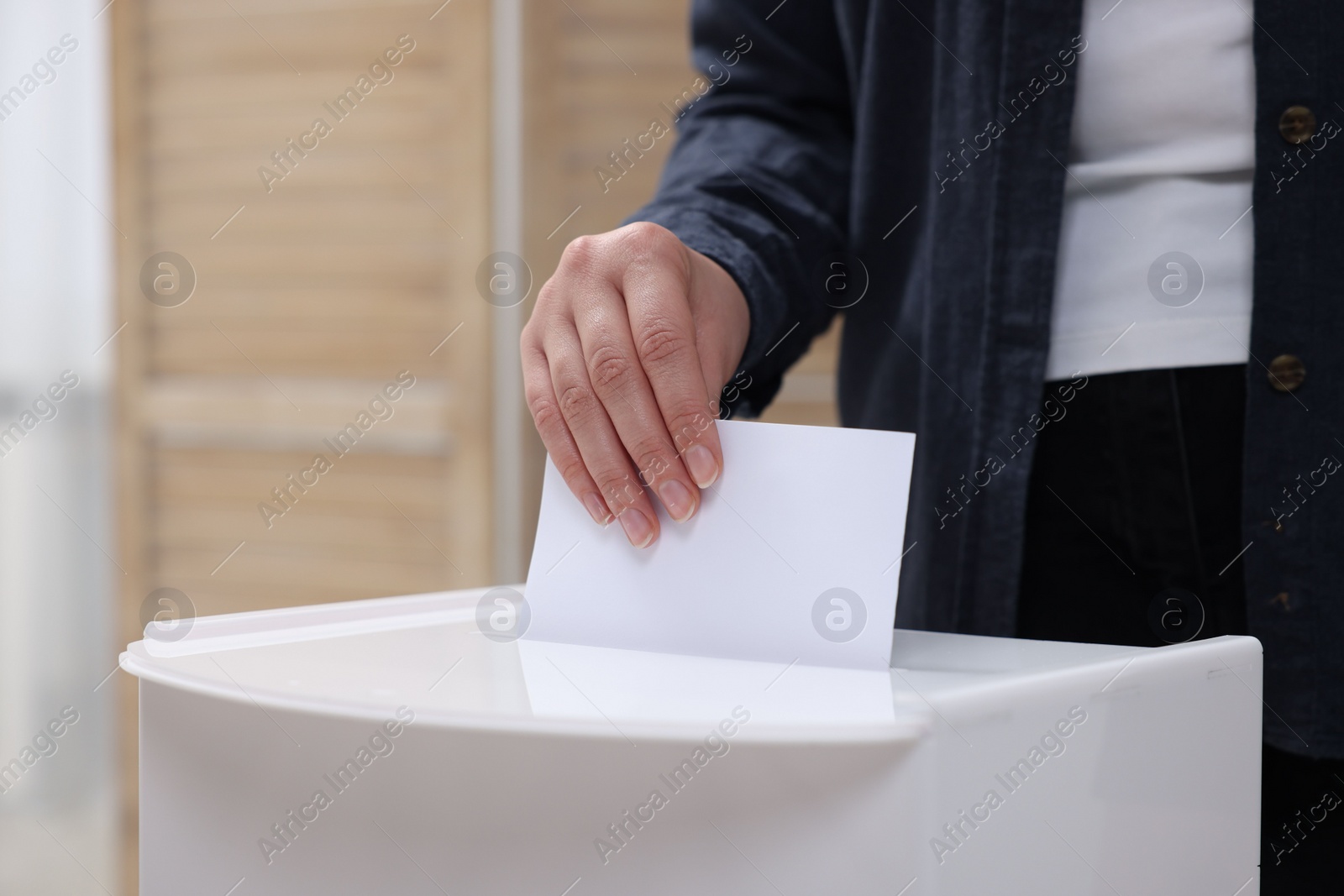 Photo of Woman putting her vote into ballot box on blurred background, closeup