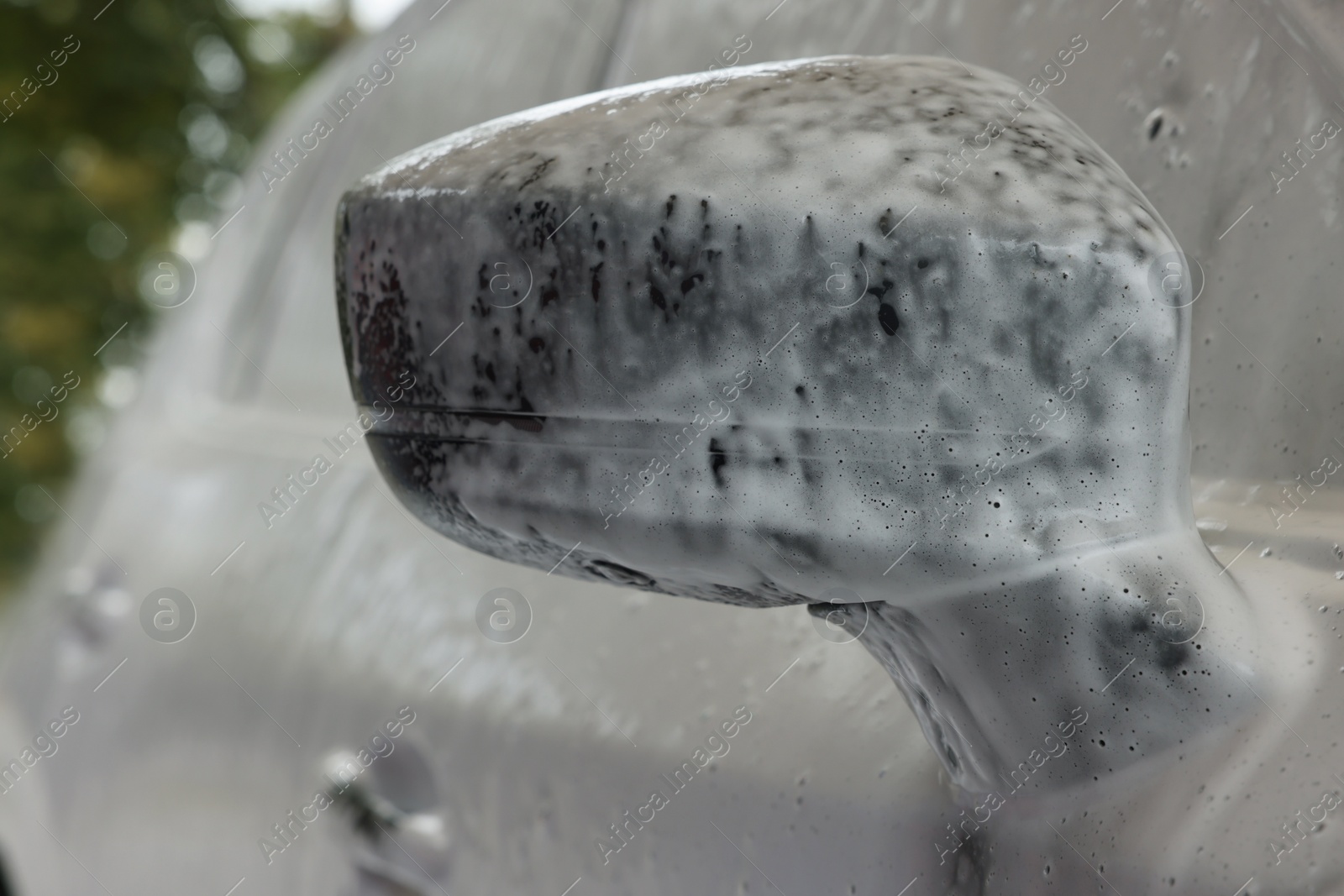 Photo of Automobile side-view mirror with cleaning foam at car wash, closeup