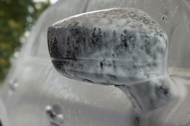 Automobile side-view mirror with cleaning foam at car wash, closeup