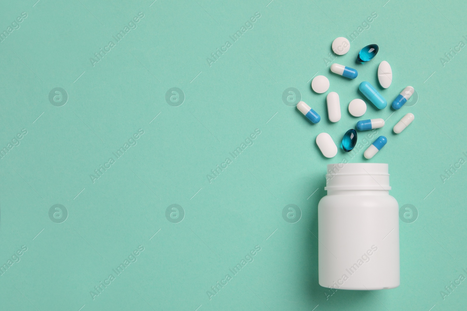 Photo of Plastic medical bottle with many different pills on turquoise background, flat lay. Space for text