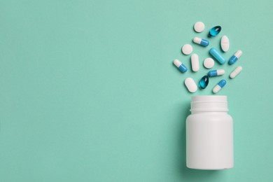 Plastic medical bottle with many different pills on turquoise background, flat lay. Space for text