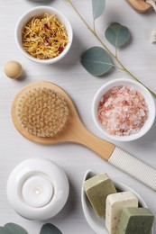 Flat lay composition with different spa products, burning candle and eucalyptus branches on light wooden table