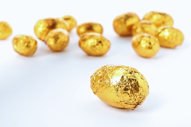 Chocolate eggs wrapped in bright golden foil on white background