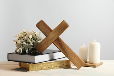 Burning church candles, wooden cross, ecclesiastical books and flowers on white table