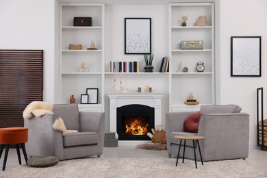Comfortable armchairs, fireplace and shelves in living room. Interior design