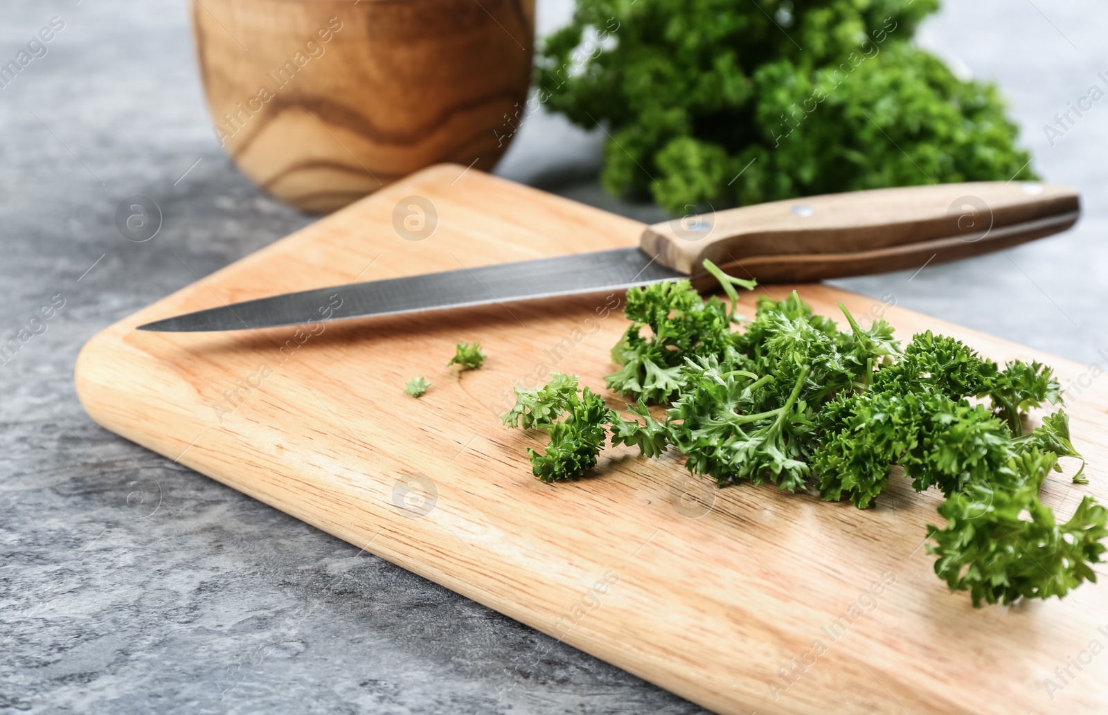 Photo of Fresh curly parsley, cutting board and knife on grey table