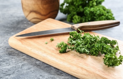 Photo of Fresh curly parsley, cutting board and knife on grey table