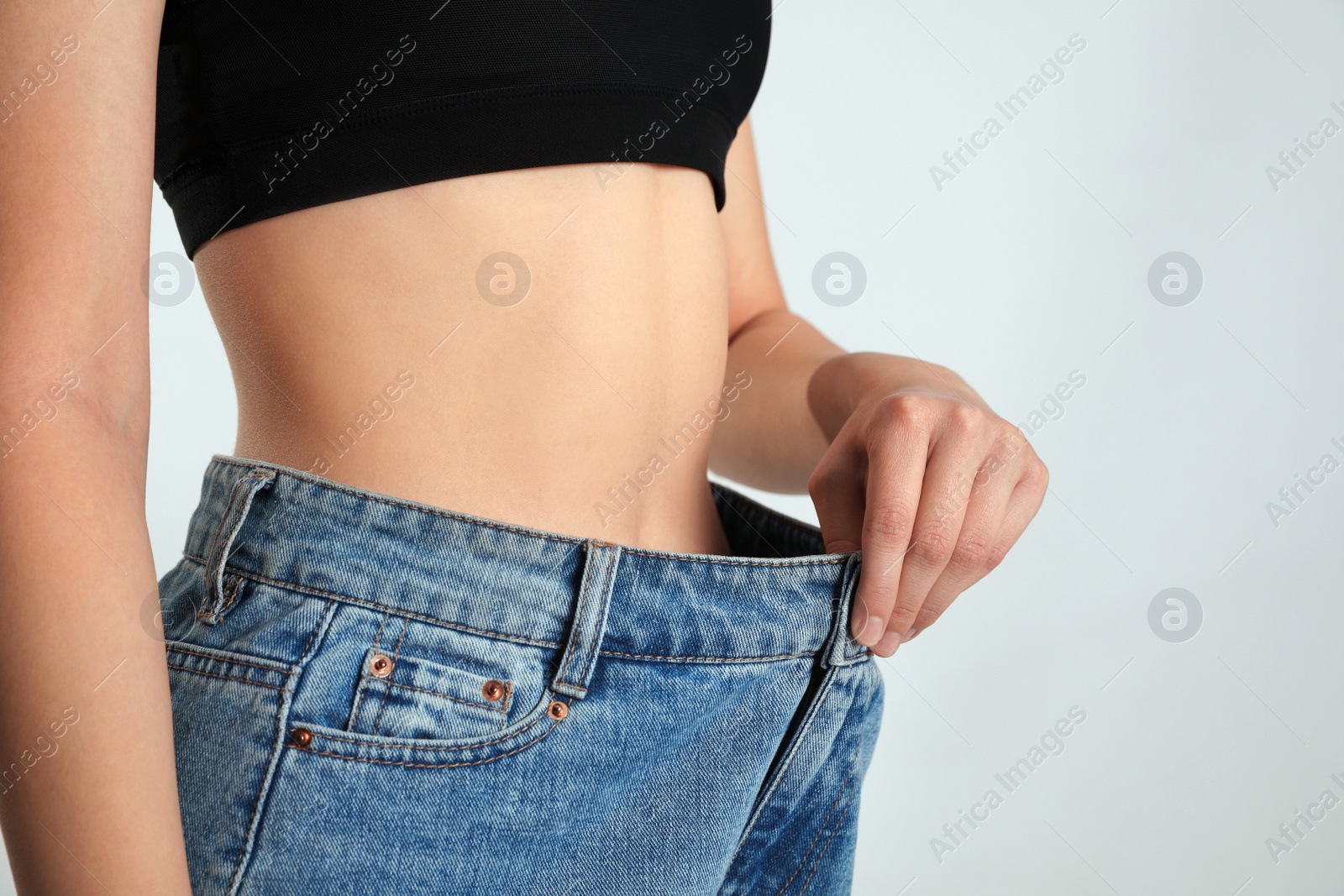 Photo of Skinny woman in oversized jeans on light background, closeup. Weight loss concept