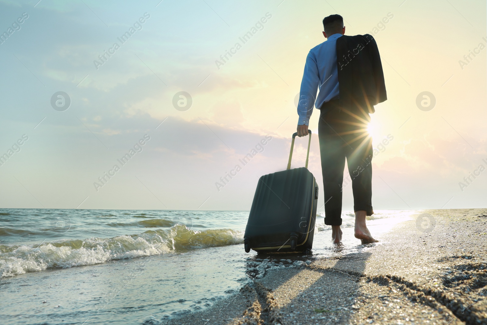 Photo of Businessman with suitcase walking on beach, low angle view. Business trip