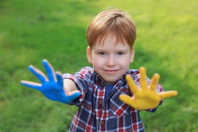 Photo of Little boy with hands painted in Ukrainian flag colors outdoors. Love Ukraine concept