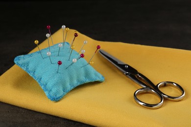 Photo of Pin cushion, yellow fabric and scissors on grey table