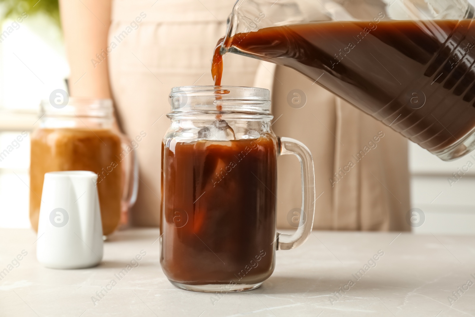 Photo of Woman pouring cold brew coffee into mason jar on table