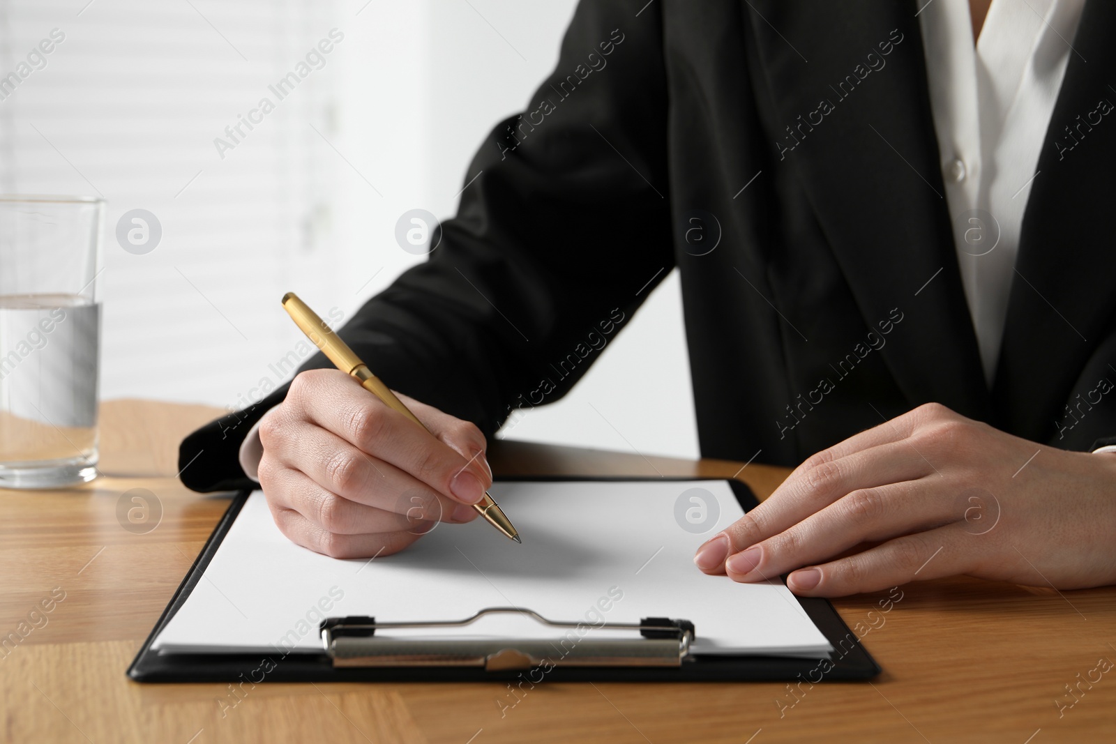 Photo of Woman with pen and clipboard at wooden table, closeup