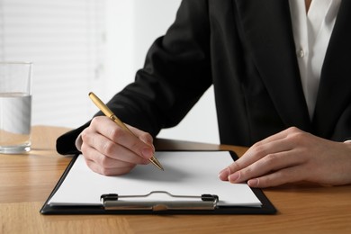 Woman with pen and clipboard at wooden table, closeup