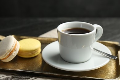 Tray with hot coffee in cup and macarons on dark textured table, closeup