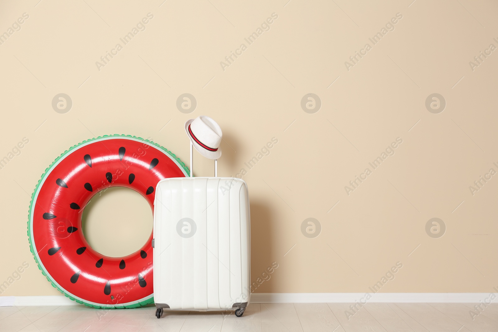 Photo of White suitcase with inflatable ring and hat near color wall. Space for text