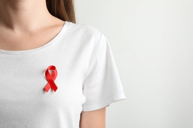 Photo of Woman with red ribbon on t-shirt against light background. Cancer awareness