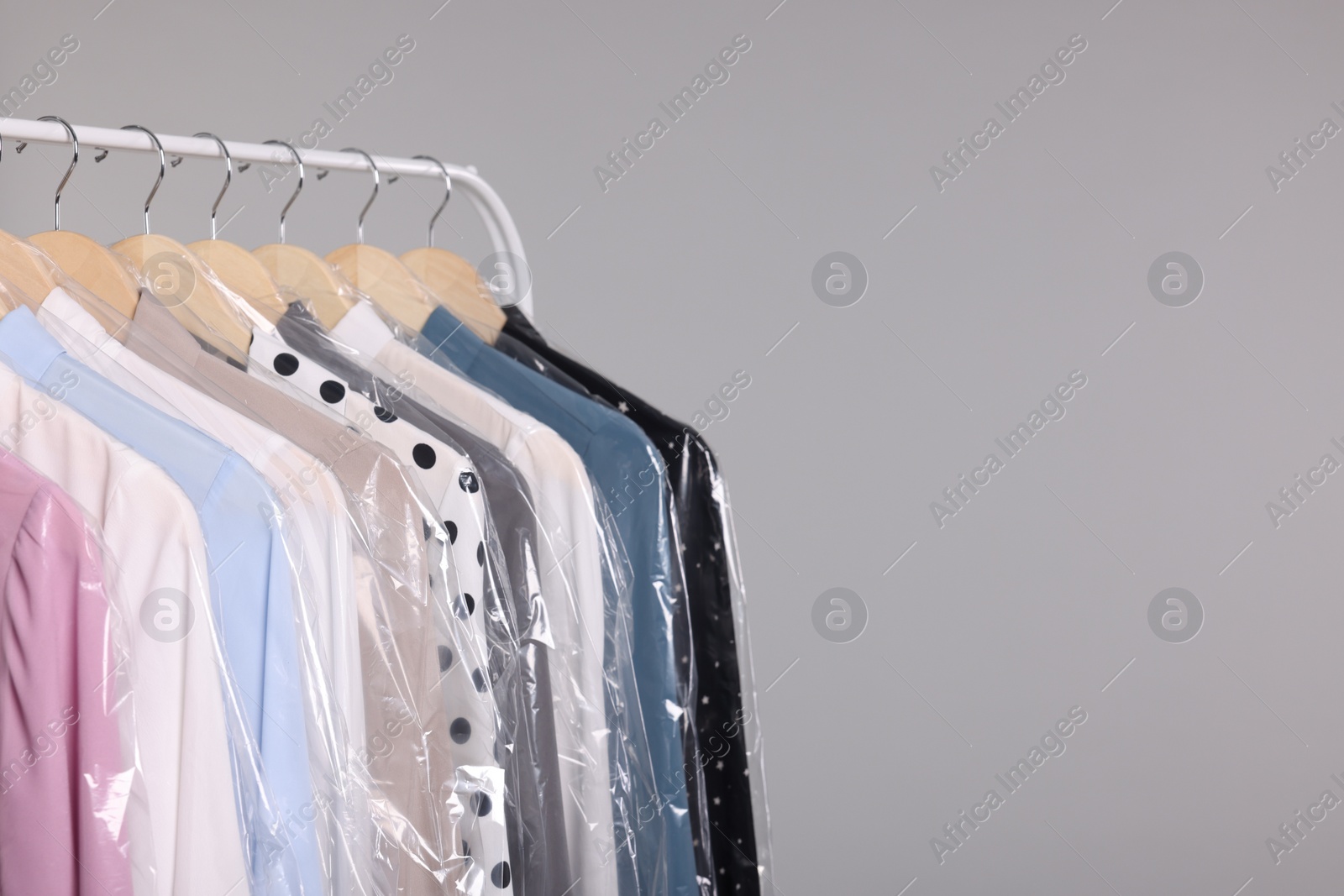 Photo of Dry-cleaning service. Many different clothes in plastic bags hanging on rack against grey background, space for text