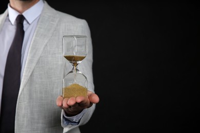 Photo of Closeup view of businessman holding hourglass on black background, space for text. Time management