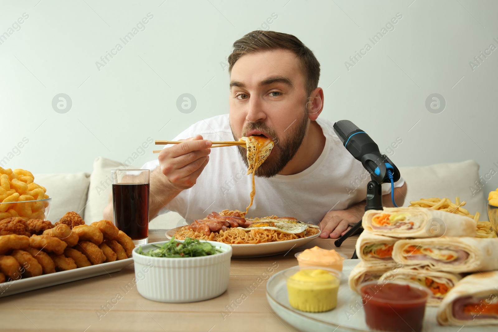 Photo of Food blogger eating in front of microphone at table against light background. Mukbang vlog