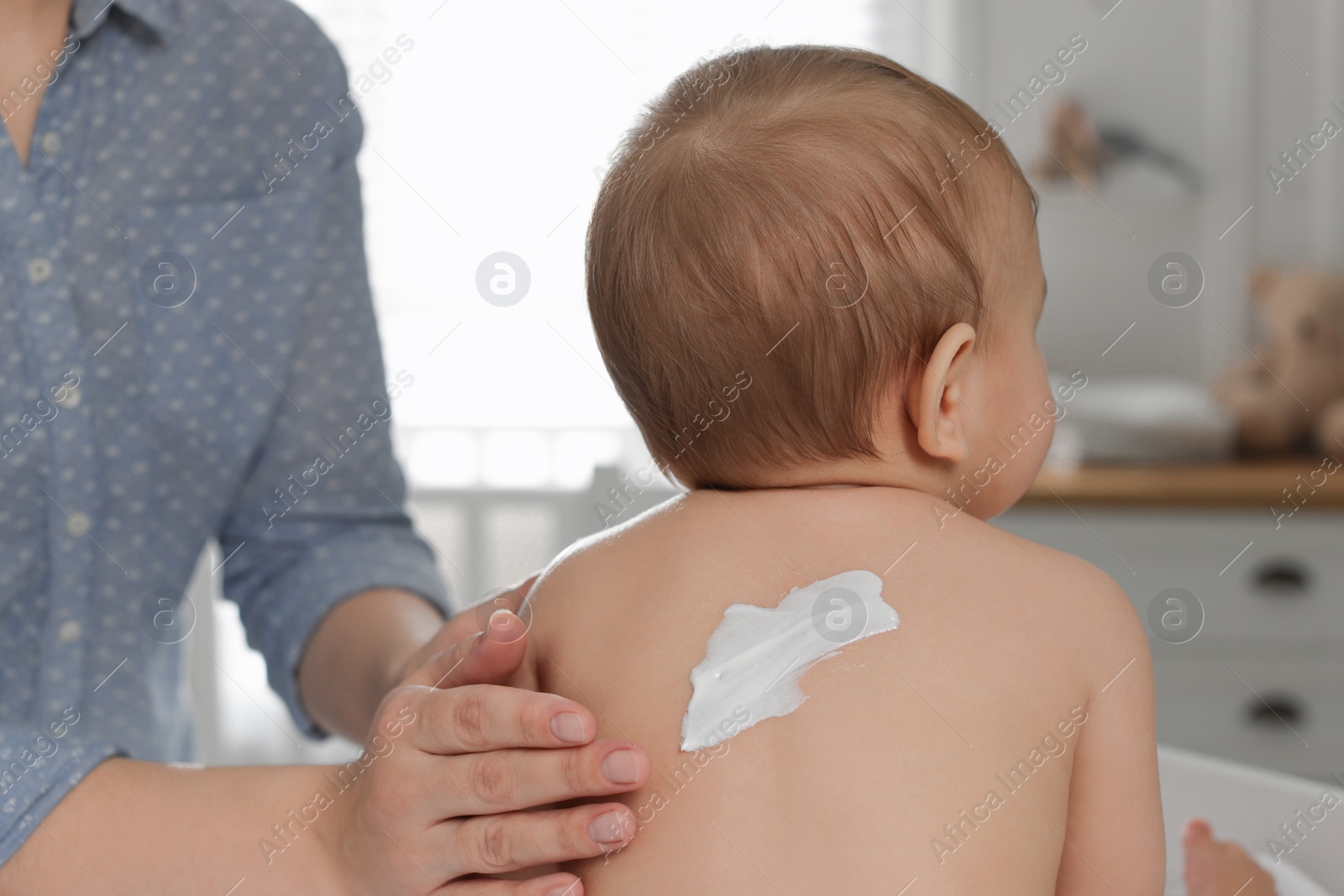 Photo of Mother applying body cream on her little baby at home, closeup
