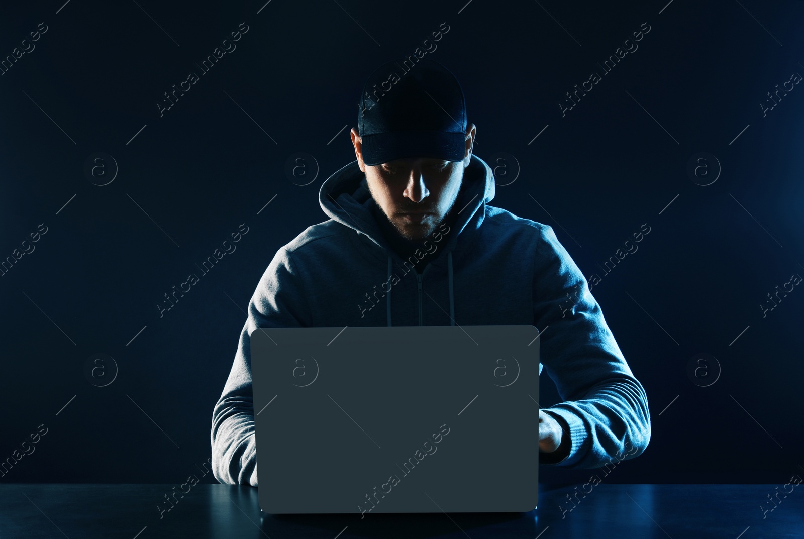 Photo of Man using laptop at table on dark background. Criminal activity