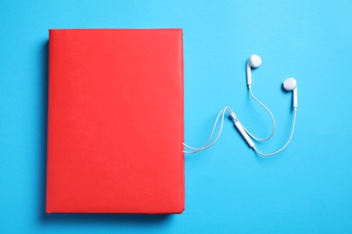 Paper book and headphones on light blue background, flat lay