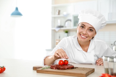 Photo of Professional female chef cooking meat on table in kitchen