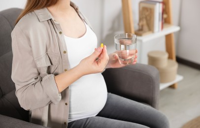 Photo of Pregnant woman holding pill and glass with water at home, closeup