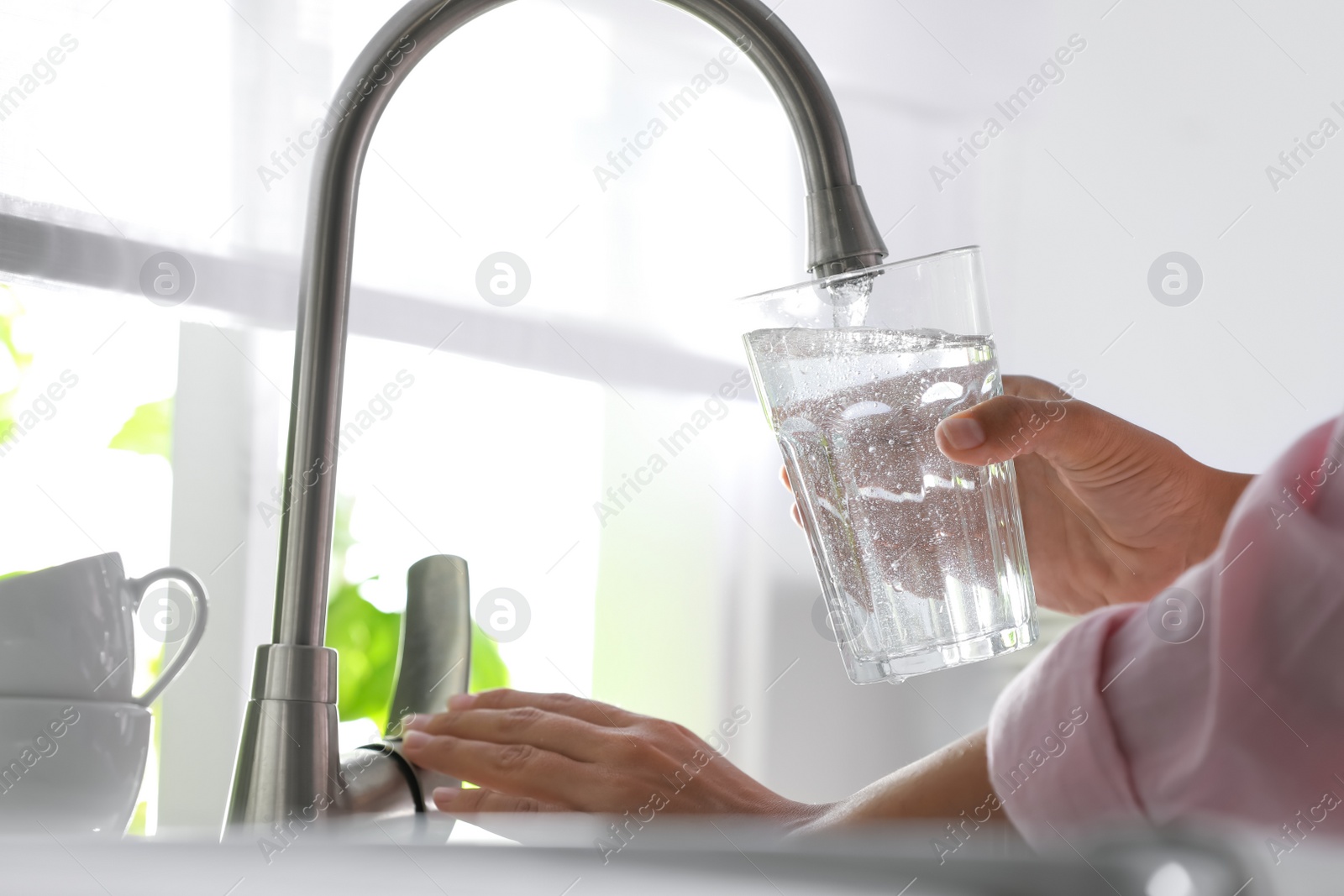 Photo of Woman pouring water into glass in kitchen, closeup