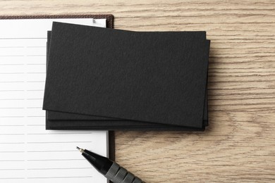 Photo of Blank black business cards, notebook and pen on wooden table, top view. Mockup for design