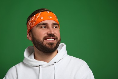 Photo of Fashionable young man in stylish outfit with bandana on green background, space for text