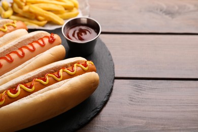 Photo of Delicious hot dogs with sauces on wooden table, closeup. Space for text