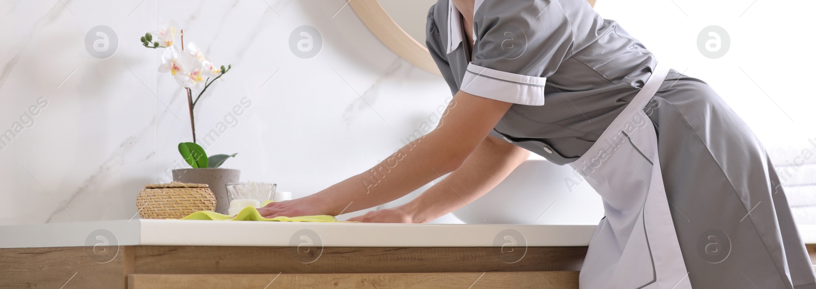 Image of Young chambermaid wiping dust from countertop in bathroom, closeup. Banner design
