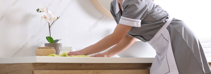 Image of Young chambermaid wiping dust from countertop in bathroom, closeup. Banner design
