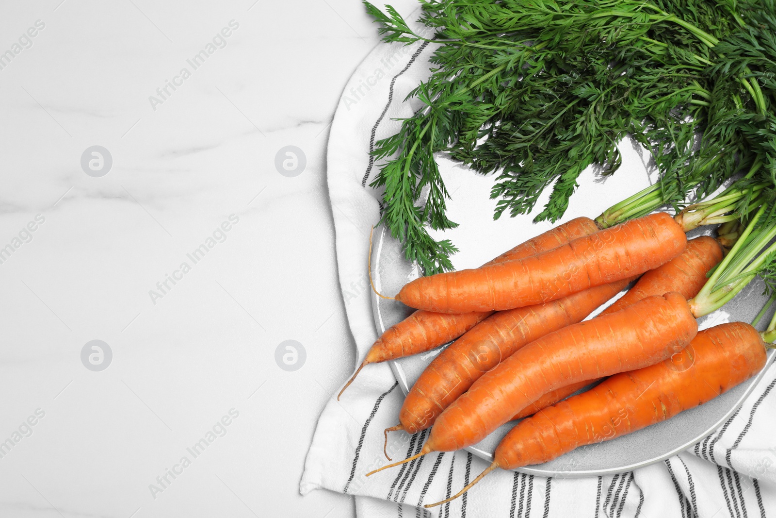Photo of Plate with tasty ripe carrots on white marble table, top view. Space for text