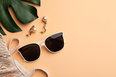 Photo of New stylish elegant sunglasses, beautiful earrings and bag on beige background, flat lay. Space for text