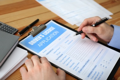 Photo of Man filling in driver's license application form at wooden table, closeup