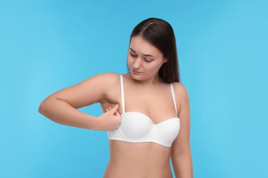 Photo of Mammology. Woman in bra doing breast self-examination on light blue background