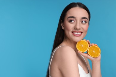 Photo of Beautiful young woman with pieces of orange on light blue background. Space for text