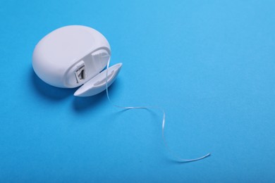 Photo of Container with dental floss on light blue background, closeup. Space for text